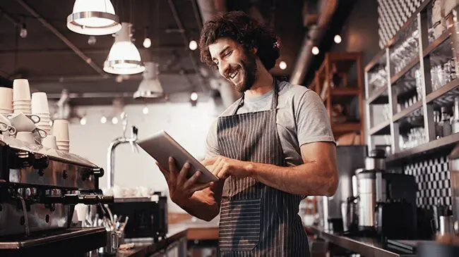 Connect-stores-and-align-management A man in an apron holding a tablet.