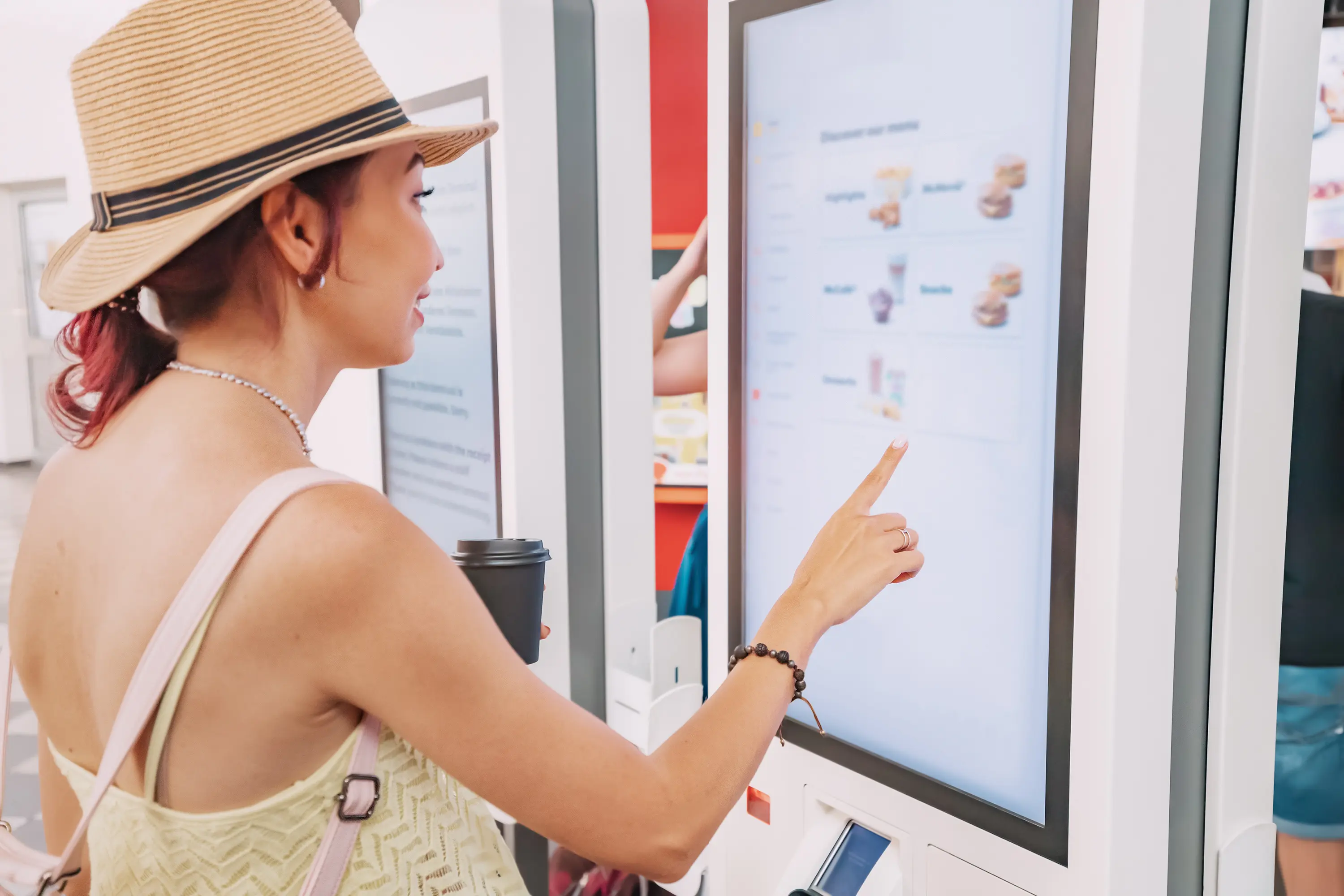 A female customer uses a touchscreen terminal or self-service kiosk to order at a fast food restaurant. Automated machine and electronic payment A woman in a hat pointing to a screen